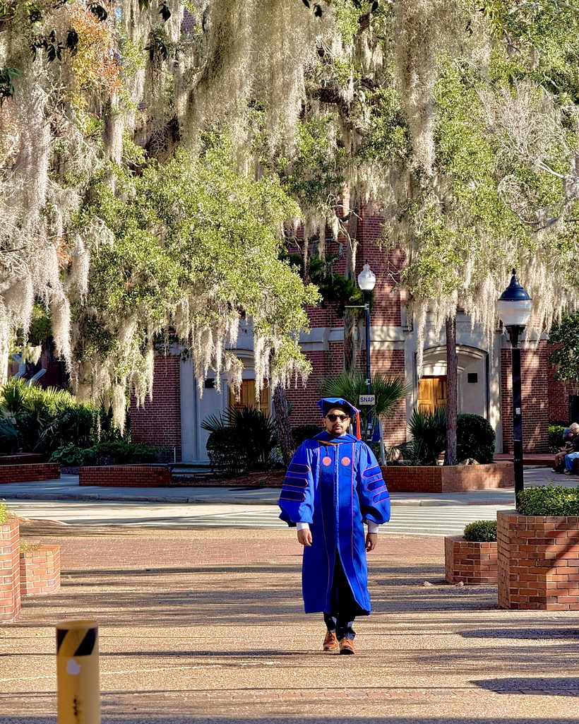 Dr. Utsab Ghimire walking through the University of Florida campus in doctoral regalia