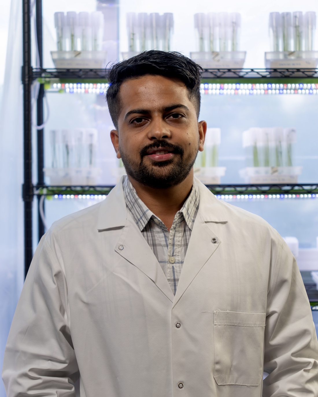 Dr. Utsab Ghimire in a lab coat in front of a plant tissue-culture rack
